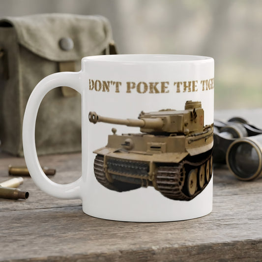 A white ceramic coffee mug printed with a tan military tank illustration and the text 'DON'T POKE THE TIGER' in brown, shown on a rustic wooden surface with blurred vintage props in the background.